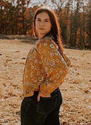 Image of Allayna L. pictured here in an orange shirt in a field. She is a student at Indiana Connections Career Academy. 